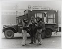 Three men drinking coffee in front of a mobile commissary truck.