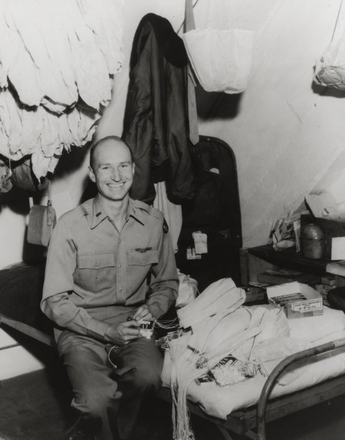 Gail Halversen sitting on a military bed tying parachutes to candy bars.