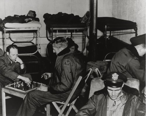 A group of men sleep on bunkbeds and play board games.