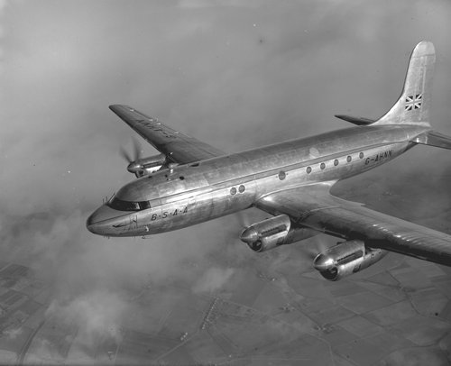 Black and white image of a four-engined propeller-driven transport aeroplane in flight.
