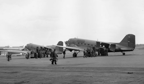 Two twin-engined transport aircraft on the ground, with people unloading supplies from side doors.