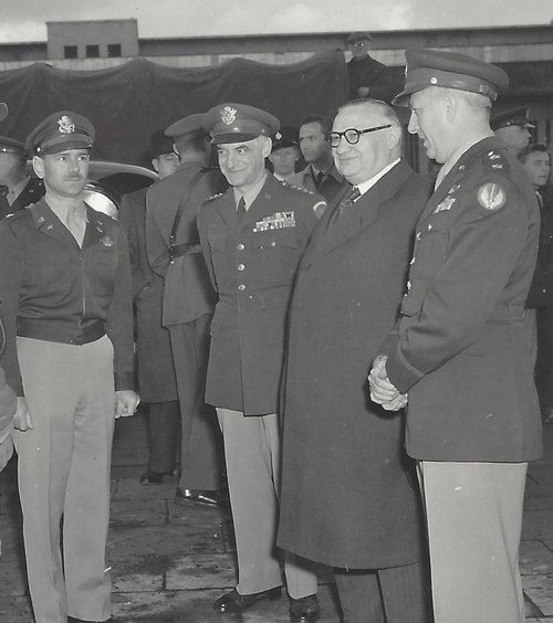Three officers in US Air Force uniform standing with a man in civilian clothes.  Other people in the background.