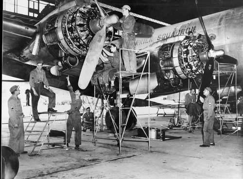 Black and white image showing men servicing a four-engined transport aircraft.