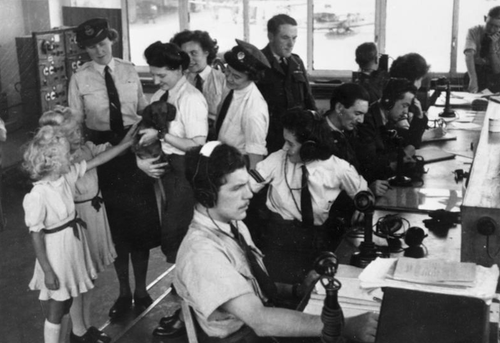 Women of the WRAF display their mascot, a dachshund named "Dakota," in the control tower building at Gatow airfield.