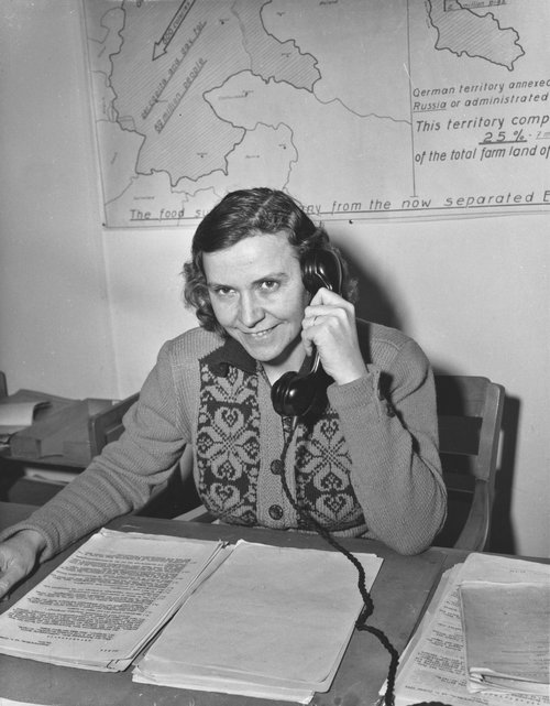 Büromitarbeiterin am Schreibtisch mit Telefonhörer in der Hand.