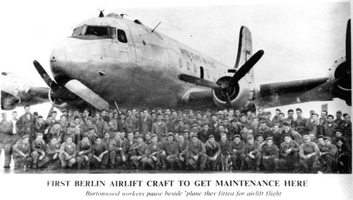 Black and white photograph showing a large number of people posing in front of a four-engined transport aircraft.