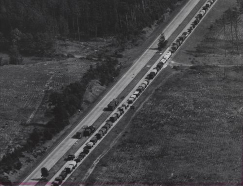 Luftaufnahme von Fahrzeugen, die auf einer Autobahn Schlange stehen. Bäume und offenes Land auf beiden Seiten.
