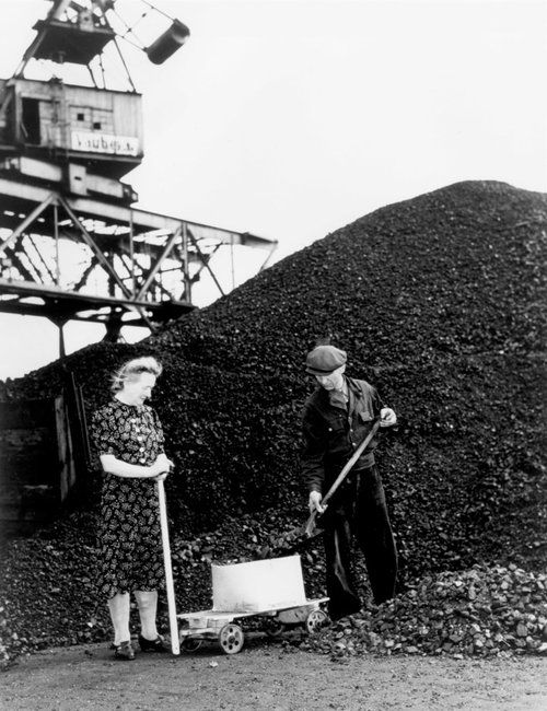 A woman with a handcart picking up her coal ration from a coal storage point. A huge pile of coal can be seen in the background.