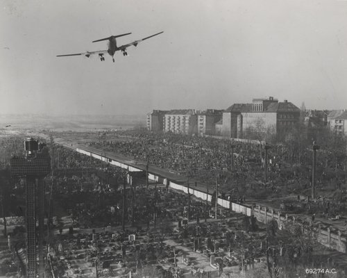 C-54 (large transport aircraft with four piston engines) flying low, rubble of Berlin below. Large six floor buildings in background
