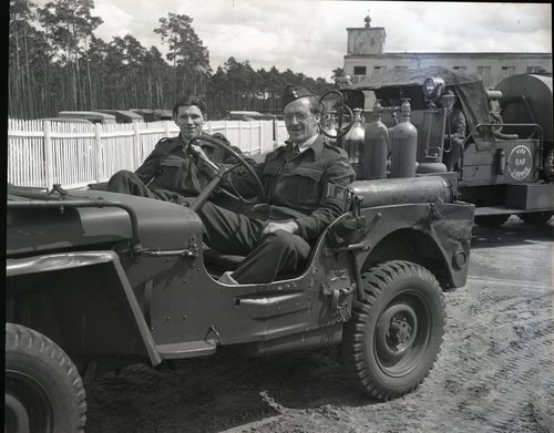 Zwei Feuerwehrleute sitzen in ihrem Einsatzfahrzeug vor der Feuerwache gegenüber vom Tower des Flughafens Gatow, Juli 1948.