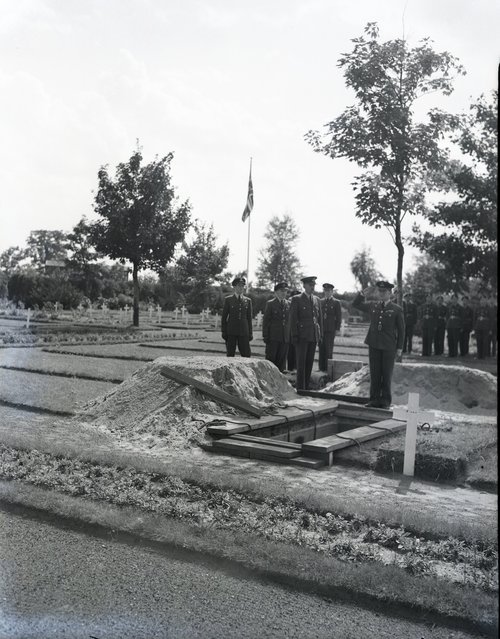 Black and white image of uniformed men standing next to a grave.