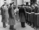 A man in RAF uniform and a woman in civilian clothes talk to men in RAF uniform, standing in line.