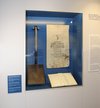 A shovel, a poster and a book in a display case.  MHM Gatow Exhibition