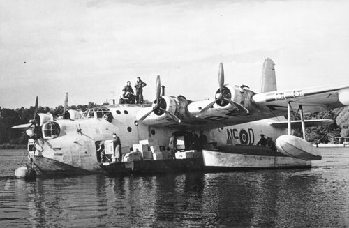 Flying boat on a lake, with men unloading boxes into a boat.