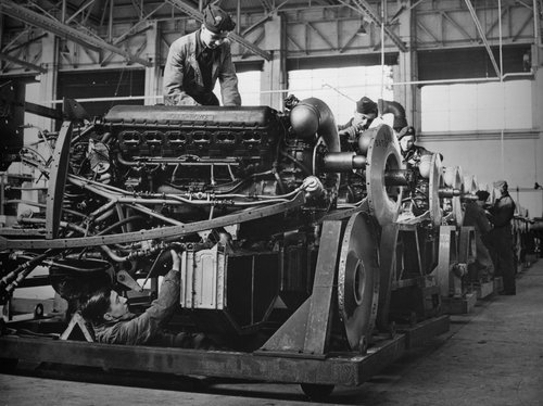 Black and white image of men working on a row of engines.