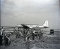Men shovelling rubble on an airfield with an aeroplane in the background.