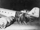 Black and white image of men moving an engine through the door of a transport aircraft.