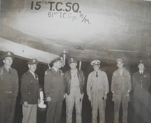 Three members of the crew and various military officials stand in front of the aircraft, which carried the two millionth ton to Berlin.