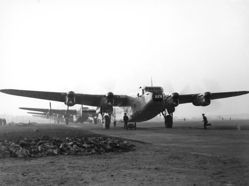 A line of four-engined transport aircraft, with engines running, queueing on an airfield.